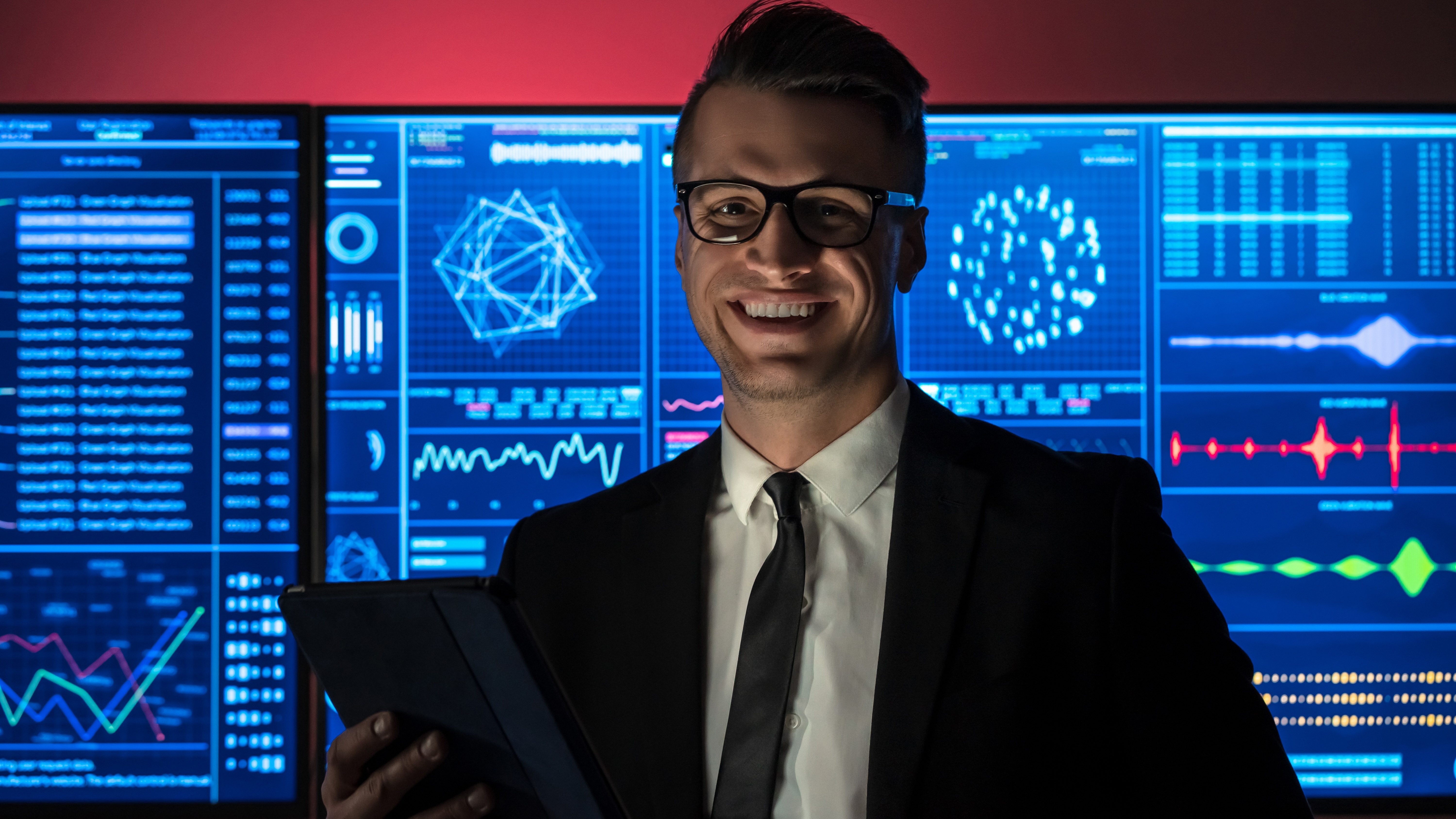 Ein Mitarbeiter zeigt die Effizient von Informationslogistik, hinter ihm Displays mit visualisierten Daten.