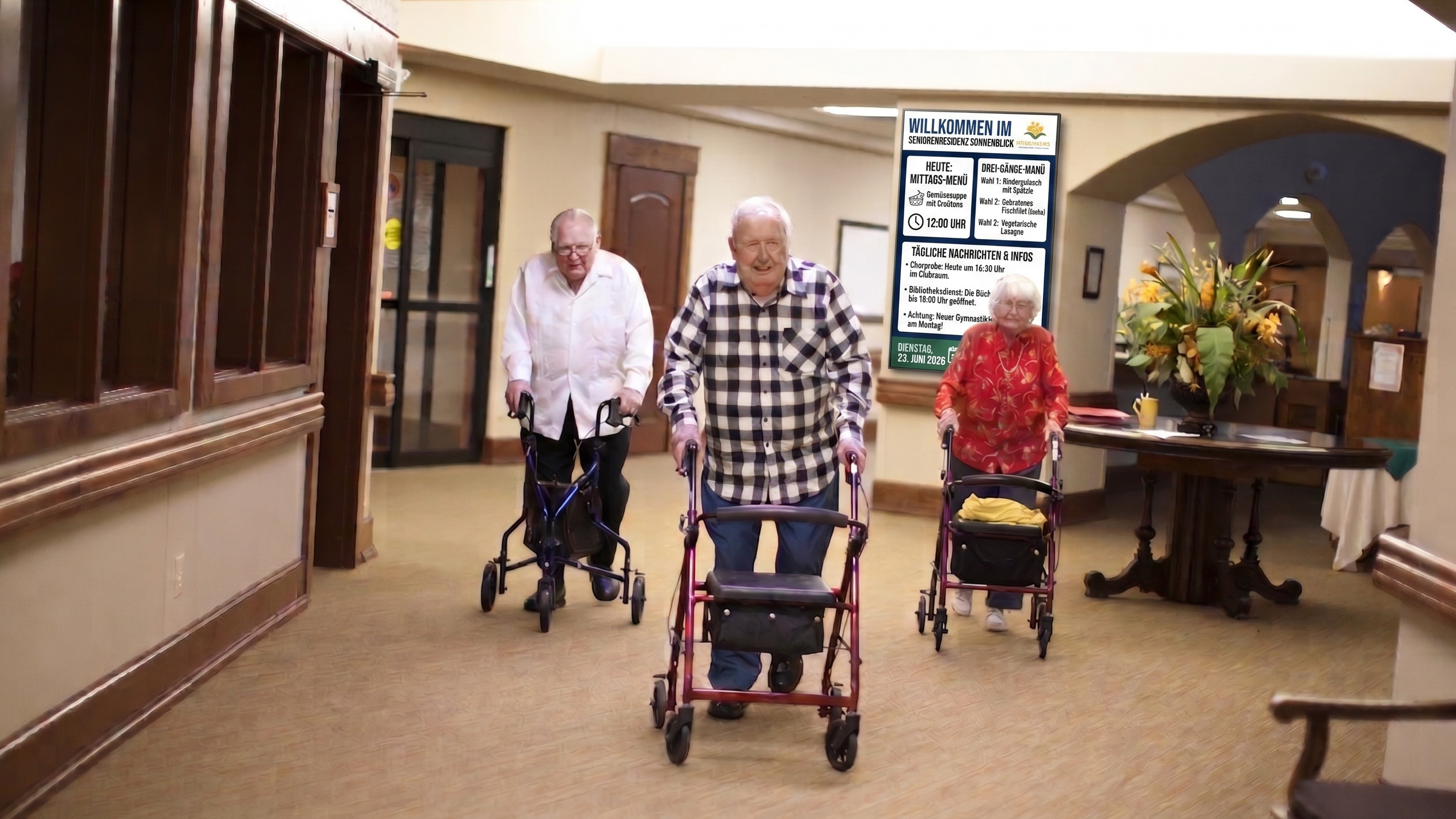 Trois personnes âgées avancent avec des déambulateurs dans le couloir lambrissé d'une résidence pour seniors ; un panneau d'affichage est accroché au mur et une composition florale orne une table.